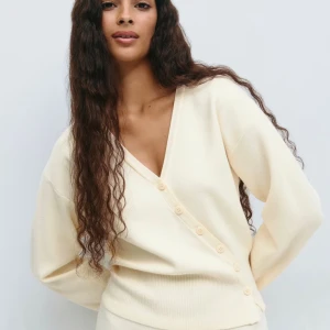 Krämvit omlottkofta med knappar - Säljer en krämvit omlottkofta med v-ringning och dekorativa knappar längs sidan. Koftan har lång ärm och ribbade muddar vid midjan. Perfekt för dig som gillar en stilren och mjuk look. Den är använd en gång och är helt ny. Ny pris 400kr men säljer för 250 pris kan diskuteras vid snabb affär.