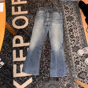 Levi's bootcut orange tab - Säljer ett par ljusblå Levi's jeans med bootcut passform och klassisk femficksdesign. Jeansen har slitningar och tvättade detaljer för en cool vintagekänsla. Materialet är robust denim och de har normal midja. Perfekt för dig som gillar retrostil.