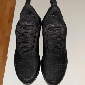 Nike Air Max 270 svarta sneakers - Svarta Nike Air Max 270 sneakers med snygg, sportig design och synlig luftkudde i hälen. Skorna har mesh-ovandel för bra ventilation, snörning och platt sula. Perfekt för dig som gillar streetstyle och vill ha bekväma skor med modern look.