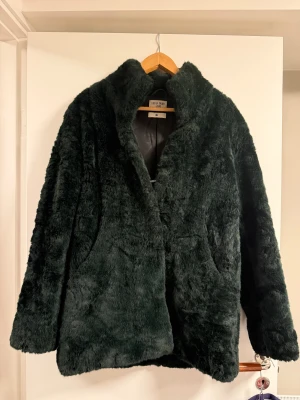 Mörkgrön pälsjacka Tiger of Sweden - Säljer en mörkgrön fuskpälsjacka från Tiger of Sweden Jeans i storlek Small. Jackan har en fluffig och mjuk yta, hög krage och två sidofickor. Perfekt för dig som vill ha en snygg och varm look under höst och vinter.