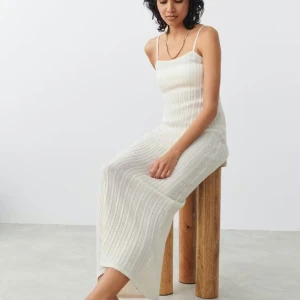 Vit ribbad långklänning från Gina Tricot  - Säljer en vit långklänning från Gina Tricot med smala axelband och ribbad stickad struktur. Klänningen är ärmlös och har en rak, slim passform som sitter snyggt mot kroppen. Perfekt för sommarens alla tillfällen, enkel att styla med smycken eller sneakers.