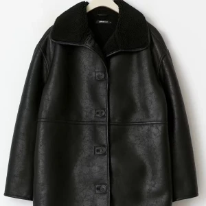 Svart teddyjacka  - Skinnjacka i läderimitation med teddykrage. Jackan är svart och har oversize fit. Den har lång ärm, knäppning och fickor i sidorna.