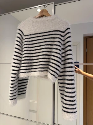 Svartvit fluffig randig tröja H&M - Supermysig fluffig tröja från H&M i vit med svarta horisontella ränder. Croppad modell med lång ärm och rund hals. Materialet är mjukt och syntetiskt, perfekt för dig som gillar cozy vibes och vill sticka ut med en cool, randig look. Lurvig vit tröja med svarta ränder i mohair liknande imitation. Mycket mjuk och skön! Semi croppad / kortare modell. Långa ärmar.  (Jeansen säljs separat i egen annons.) Storlek XS-S.