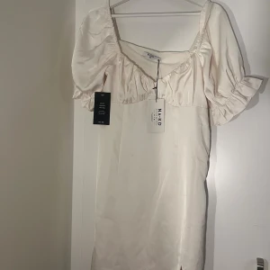 Champagnefärgad kort klänning NA-KD - Superfin vit kort klänning från NA-KD med puffiga korta ärmar, v-ringning och liten slits framtill. 