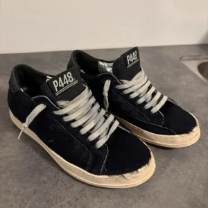 Svarta sneakers från P448 med päls - Unika svarta sneakers från P448 med pälsliknande yta och kontrasterande vita snören. Skorna har en rund tå, platt sula i beige och svart, samt silverdetaljer vid hälen. Märket syns tydligt på tungan. Perfekt för dig som gillar att sticka ut med din stil.