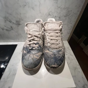 Maison marigela gats  sneakers, vit/blå, stl 41 - Säljer ett par unika Maison marigela gats sneakers i vit canvas med blå färgstänk och slitna detaljer. Skorna har snörning, rund tå och platt sula. Coolt distressed utseende . Dock så är dem slitna där fram på ena skon och i hälen har de gått upp som man kan se i en av bilderna priset går att diskuteras vid snabb affär hör av vid minsta fråga !!!