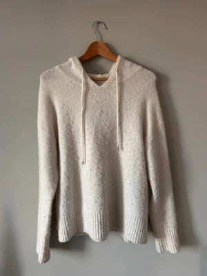 Vit stickad hoodie från Primark - Mysig vit stickad hoodie från Primark med huva och snörning. Tröjan har långa ärmar och ribbade muddar vid ärmslut och nederkant. Perfekt för chilliga dagar och har en loose passform som ger en avslappnad vibe.