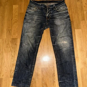 Blå  jeans från Nudie Jeans - Snygga mörkblå jeans från Nudie Jeans med slitna detaljer och kontrastsömmar. Klassisk femficksmodell med raka ben och coola slitningar framtill och på bakfickorna. Perfekta för en avslappnad streetstil.