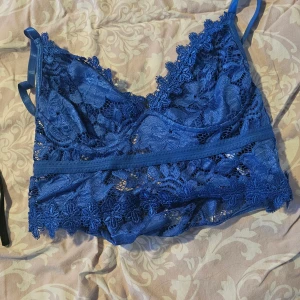 Blå spetsig linnetopp med smala band - Säljer en snygg blå linnetopp i spets med smala axelband och v-ringad hals. Toppen har genomgående blommigt spetsmönster och dekorativ kant nertill. Perfekt för dig som gillar detaljer och vill ha en feminin look.