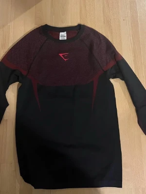 Long sleeve Gymshark onyx v5 - Snygg långärmad träningströja från Gymshark i svart med vinröda detaljer och grafiskt mönster på axlar och rygg. Tröjan har en slim passform och är gjord i mjukt syntetmaterial som andas bra. Perfekt för gymmet eller sportaktiviteter. Kan tänka mig gå ner i pris vid snabb affär. Helt ny skick aldrig använd. Säljer då den inte passade