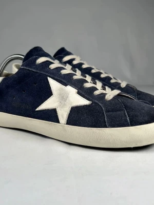 Mörkblå sneakers från Golden Goose - Snygga mörkblå sneakers från Golden Goose med vit stjärndetalj på sidan och vita snören. Ovandelen är i mocka och sulan är vit med svart undersida. Perfekta för dig som gillar en cool och avslappnad stil.