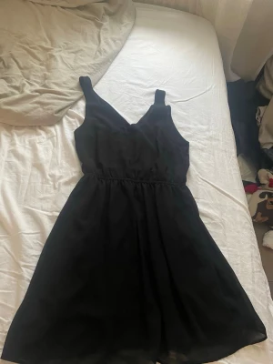 Svart kort klänning från H&M Divided - Säljer en svart klänning från H&M Divided i storlek 38. Klänningen har v-ringad hals, ärmlös design och markerad midja. 