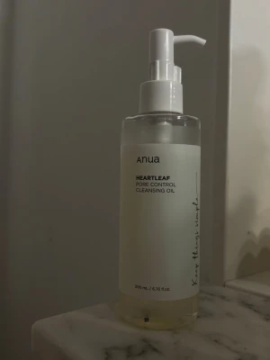 Anua Heartleaf Cleansing Oil - Anua Heartleaf Pore Control Cleansing Oil i en genomskinlig plastflaska med vit pump. Innehåller 200 ml rengöringsolja som är ljusgul. Perfekt för att ta bort smink och rengöra porerna. Enkel och stilren design med svart text på etiketten. Använt fåtal gånger (3 tillfällen). 
