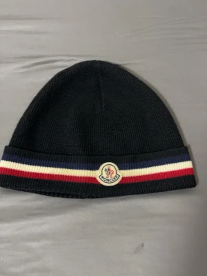 Svart Moncler mössa med ränder - moncler mössa den är använd men inga skador på den inga brännskador eller något sånt den är äkta och har nfc scan inne och tar byten bror på vad det är och pris kan alltid diskuteras .
