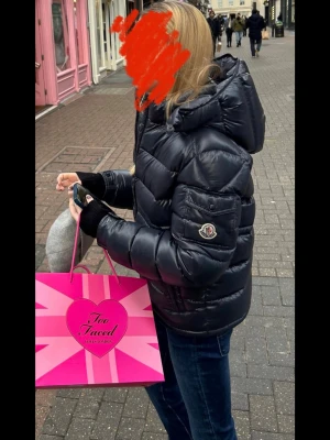 Svart Moncler pufferjacka med huva - Säljer en svart pufferjacka från Moncler med stor huva och snygga quiltade paneler. Jackan är äkta, innehåller QR kod och är inköpt på Smultronet i Djursholm för 9635 kr för 2 år sedan. Den har dragkedja framtill, två sidofickor med dragkedja och Moncler-logga på ärmen. Så snygg och perfekt för alla tillfällen. 