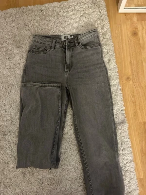Grå split jeans från 157 - Unika grå jeans från 157 med split-design på ena benet. Modellen har klassisk femficksdesign, hög midja och raka ben. Jeansen är tillverkade i slitstarkt bomullsmaterial och har en cool, mörkgrå ton som passar till streetwear och trendiga outfits.