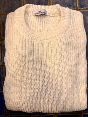 Vit stickad tröja från Stone Island - Vit stickad tröja från Stone Island med klassisk rund hals och ribbade muddar. Tröjan har den ikoniska Stone Island-patchen på höger ärm. Materialet är grovstickat och är definitivt en high end-produkt. Testad, aldrig använd. Tröjan kan självklart lämnas in till Instabox redan idag för blixtsnabb leverans. Perfekt julklapp!