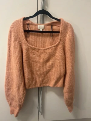 Croppad stickad tröja från H&M - Säljer en ljusrosa croppad stickad tröja från H&M i storlek XS. Tröjan har en bred, fyrkantig ringning och långa ärmar med lätt puff. Ribbad struktur ger en mysig känsla och passar perfekt till jeans eller kjol. Passar upp till storlekarna S/M.