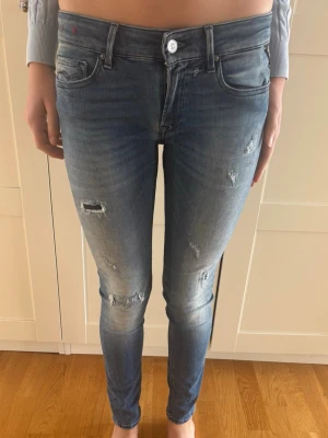 Blå skinny jeans med slitningar Replay 27/32 - Säljer ett par blå Replay jeans med skinny fit och låg midja. Jeansen har slitna detaljer och snygg tvätt med ljusare partier på låren och knäna. Klassisk femficksmodell och stretchigt material som sitter tajt och bekvämt. Väldigt fint skick! 