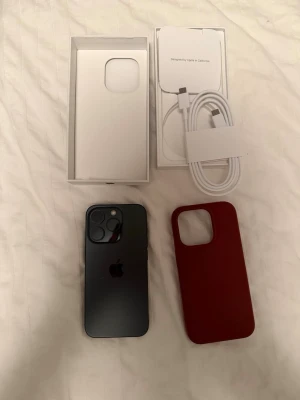 iPhone 15 Pro - Snygg iPhone 15 Pro i svart, komplett med originalkartong, USB-C kabel och brun MagSafe-kompatibel skal från Ideal of Sweden. Telefonen har väldigt små tecken på användning och har 82% batteri hälsa