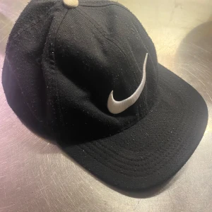 Nike Classic-99 Keps - Svart keps från Nike med stor vit Swoosh-logga på framsidan och broderad Nike-text bak. Klassisk modell med böjd skärm och justerbar passform. Tillverkad i Dri-FIT-material som andas.