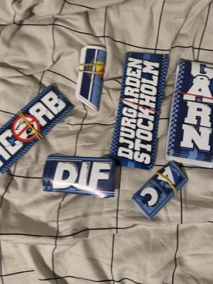 Blå och vita Djurgården stickers 70st - Säljer ett gäng feta stickers med Djurgården-tema i blått och vitt. Motiven är bland annat DIF-logga, Djurgården Stockholm och coola grafiska tryck. Perfekt för att pimpa laptop, mobil eller väskan. Alla stickers är buntade med gummiband. Du kan stötta Djurgården med att köpa och att gå runt och sätta de i din stad 