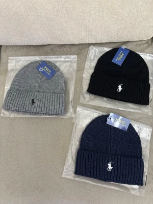 Tre polo mössor. Top kvalité  - Bilden visar tre stickade mössor från Polo Ralph Lauren i grått, svart och marinblått, med broderad logga framtill. Ingen väst syns på bilden. 1 kostar 250 2 kostar 450 3 kostar 550