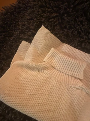 Beige stickad polotröja - Säljer en beige stickad polotröja med bred, vikt krage. Sytt ihop sidorna själv. Tröjan har en klassisk rak passform och är ribbstickad för extra struktur. Perfekt för lager på lager under kyliga dagar. Enkel och stilren design som passar till det mesta.