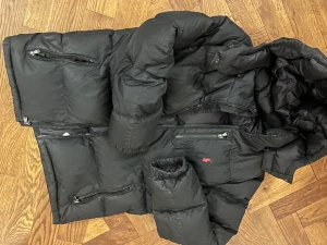 Svart pufferjacka Polo Ralph Lauren XL - Svart pufferjacka från Polo Ralph Lauren i storlek 170 (största barnstorlek). Jackan har flera dragkedjeförsedda fickor, huva och ett litet rött Polo-logomärke på bröstet. Materialet är syntet och polyester, perfekt för kalla dagar. Snygg och praktisk design med långärmade ärmar. Ett litet hål i ena fickan.