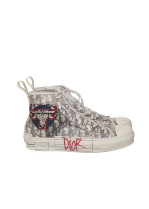 Dior B23 sneakers med tjurpatch - Snygga Dior B23 high-top sneakers i vitt och grått med genomskinlig textil, monogrammönster och röd broderad tjurpatch på sidan. Sulan har röd Dior-logga och skorna har vita snören och gummisula. Perfekt statement-piece för dig som gillar streetstyle.