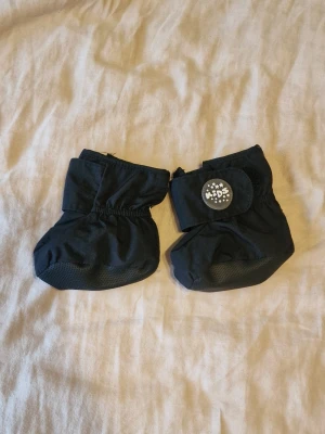 Svarta fleecefodrade tossor med kardborre - Säljer ett par svarta tossor för barn med mjukt fleecefoder och kardborreband. Sulan har halkskydd och tossorna har reflexdetaljer för extra synlighet. Perfekt för kalla dagar.