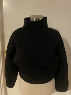 Svart polotröja med loose fit - Svart polotröja med hög krage och långärmad design. Tröjan har en loose passform och är tillverkad i ett mjukt material som känns skönt mot huden. Perfekt för dig som gillar enkel och stilren look med lite extra edge.