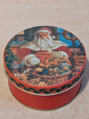 Burk med julmotiv  - Burk av metall med julmotiv. Jätte fin metallburk med en jultomte som julmotiv. På sista bilden visas en bild med en jätte liten defekt, färgen saknas på en jätte liten bit