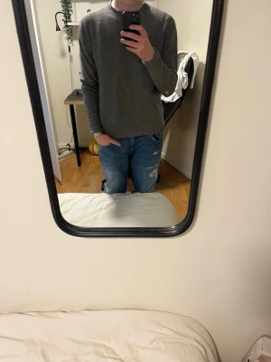 Grå stickad tröja med rund hals - Säljer en enkel och stilren grå stickad tröja med rund hals. Tröjan har långärmade ärmar och en normal passform, perfekt för att hålla dig varm under kyliga dagar. Passar bra till jeans och sneakers för en avslappnad look. Litet hål i armen syns på bilden.