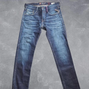 Replay Anbass FC Barcelona jeans - Snygga blå jeans från Replay Anbass FC Barcelona edition, tillverkade i Italien. Klassisk femficksmodell med raka ben och coola detaljer som FC Barcelona-logga och Replay-märke bak. Jeansen har kontrastsömmar och slitningar för en schysst look.