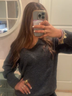 Mörkgrå stickad tröja med v-ringning - Mysig mörkgrå stickad tröja med avslappnad passform och v-ringad hals. Perfekt för lager-på-lager och enkel att matcha med olika outfits. Tröjan har långa ärmar och är tillverkad i ett mjukt, stickat material. Använder inte den för att jag personligen inte gillar färgen på mig. 