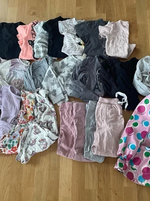 Stort klädpaket storlek 110/116 - Säljer ett stort klädpaket med flera t-shirts, långärmade tröjor, leggings och shorts i olika färger och mönster. Här finns motiv som enhörningar, hjärtan och blommor samt enfärgade plagg i svart, grått, rosa och lila. Perfekt för dig som vill ha en varierad garderob!