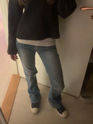 Blå low waist bootcut jeans - Säljer ett par ljusblå bootcut jeans med slitningar och hål på knäna. Vet tyvärr inte märket då de är min mammas gamla, nypris 1200kr💕