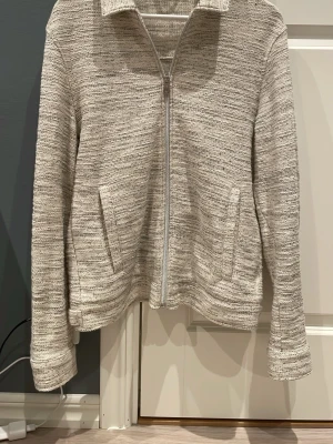 Beige ziptröja med krage - Snygg beige ziptröja med krage och två fickor framtill. Tröjan har en fin struktur och raka ärmar. Perfekt för våren och enkel att matcha med olika outfits.