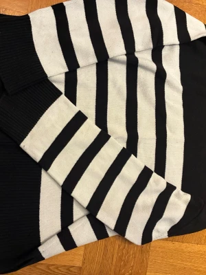 Svartvit randig stickad tröja - Snygg stickad tröja med breda svarta och vita ränder. Tröjan har långa ärmar och ribbstickade muddar vid ärmslut och hals. 