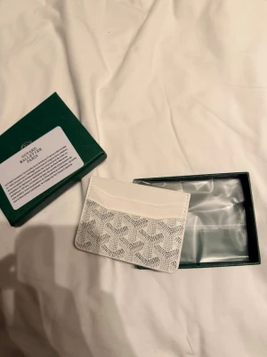 Vit kortfodral  - Säljer ett stilrent vitt kortfodral  med deras ikoniska mönster i grått. Kortfodralet har flera fack för kort och är tillverkat i läder med canvasdetaljer. Perfekt för dig som vill ha en exklusiv accessoar i fickan.