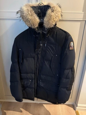  Parajumpers dunjacka  - Snygg svart dunjacka från Parajumpers med stor huva och fluffig pälskant. Jackan har flera fickor framtill, patch på ärmen och klassisk quiltad design. Perfekt för kalla vinterdagar och riktigt varm. De är storlek S men passar även M