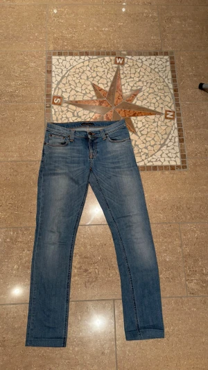 Nudie Jeans w27 L34  passar L32 - Snygga blå slim fit jeans från Nudie Jeans med klassisk femficksdesign och subtila slitningar på låren. Jeansen har normal midja och raka ben, perfekta till en avslappnad stil. Tillverkade i mjuk denim med en autentisk tvätt.