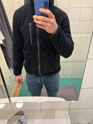 Hansen&Jacon fleecejacka  - Mysig mörkblå fleecejacka med hög krage och hel dragkedja framtill. Jackan har tre fickor med dragkedja, två framtill och en på bröstet. Perfekt för kyliga dagar och har en avslappnad passform.