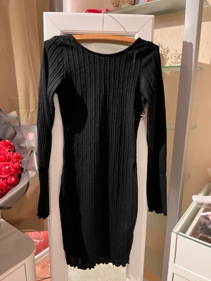 Svart ribbad långärmad klänning - Snygg svart ribbad klänning med lång ärm och rundad halsringning. Klänningen är figurnära och längden är till knä. Materialet är stretchigt och bekvämt. Klänningen är helt ny med prislappen.