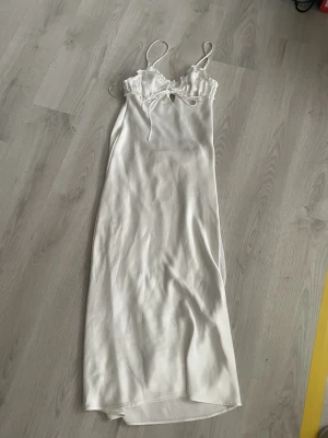 Vit långklänning i satin med snören  -  vit långklänning i satin med smala axelband och snören i fram. Klänningen har en mjuk glansig yta. Från Zara, köpt för cirka 3 år sen men knapp andvönd 