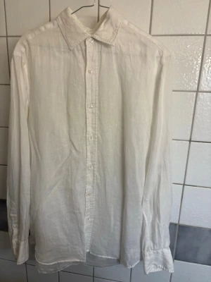 Vit linneskjorta - Klassisk vit skjorta i linne från Massimo Dutti med lång ärm och knäppning framtill. Skjortan har en avslappnad passform och enkel krage, perfekt för en clean och stilren look. Passar lika bra till jeans som till shorts.