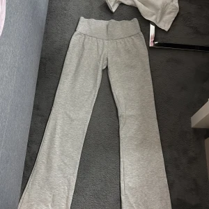 Grå mjukisbyxor från Nelly - Snygga grå mjukisbyxor från Nelly med utsvängda ben och bred, ribbad midja. Mjukt och bekvämt material. ENDAST ANVÄND 2 gånger