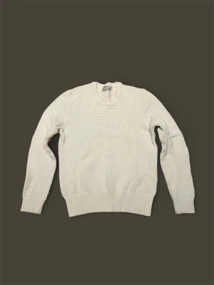 Beige stickad tröja från Acne Studios - Säljer en beige stickad tröja från Acne Studios med rund halsringning och grovstickad struktur. Tröjan har långa ärmar och breda ribbade muddar vid ärmslut och nederkant. Perfekt för lager på lager och enkel att matcha. Tröjan har en nästan omärklig liten fläck på baksidan och har även blivit färgad av jeans på insidan, detta syns dock inte när man har på sig tröjan.