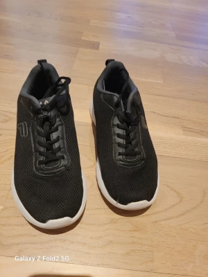 Svarta sneakers från Fila - Snygga svarta sneakers från Fila med vit sula och mesh-överdel. Skorna har klassisk låg profil, svarta skosnören och diskret Fila-logga på sidan. Perfekta för en sportig och avslappnad stil. Lätta och bekväma att bära hela dagen.